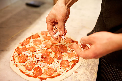 food, culinary, italian cuisine, people and cooking concept - cook hands adding ham to salami pizza at pizzeria