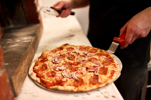food, italian cuisine, people and cooking concept - cook with pizza peel and cutter at pizzeria