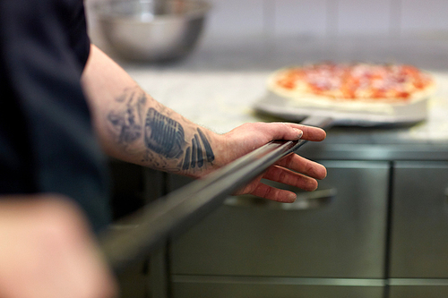 food cooking, culinary and people concept - cook or baker hand with pizza on peel at pizzeria