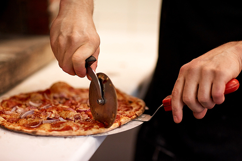 food, italian kitchen and cooking concept - cook hands with cutter cutting pizza to pieces at pizzeria