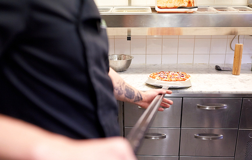 food cooking, culinary and people concept - cook or baker hands with pizza on peel at pizzeria