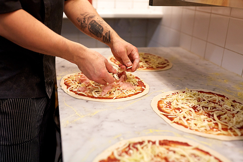 food cooking, culinary and people concept - cook or baker hands adding champignons to pizza at pizzeria