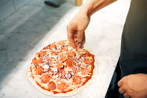 food, culinary, italian cuisine, people and cooking concept - cook hands adding red onion to salami pizza at pizzeria
