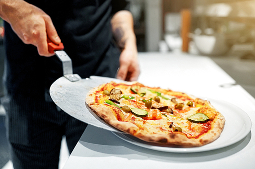 food cooking, culinary and people concept - cook or baker placing pizza from peel to plate at pizzeria