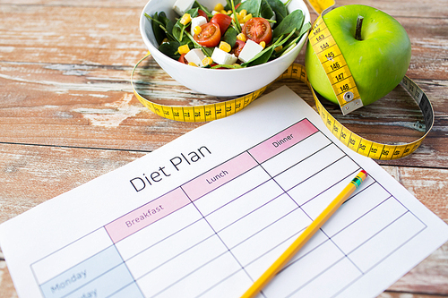 healthy eating, dieting, slimming and weigh loss concept - close up of diet plan paper with green apple, measuring tape and salad