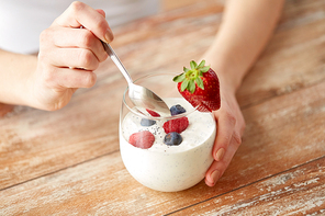 healthy eating, food and people concept - close up of woman hands with yogurt and berries in glass on table