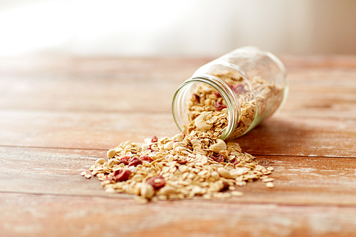 food, healthy eating and diet concept - jar with granola or muesli poured on wooden table