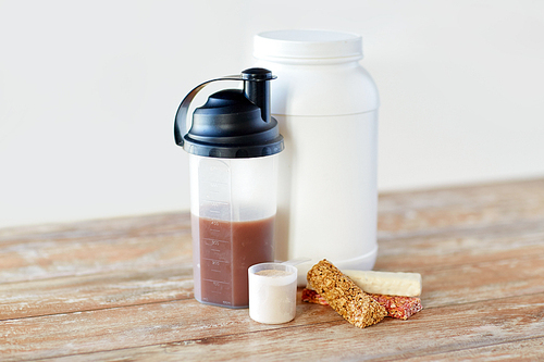 sports nutrition, fitness diet and food concept - jar, protein shake bottle and muesli bars on wooden table