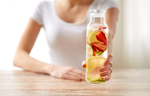 healthy eating, detox and people concept - close up of woman with fruit water in glass bottle at home