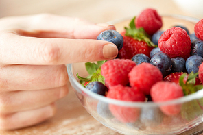 healthy eating, vegetarian food and people concept - close up of young woman hand with berries in glass bowl