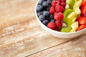 healthy eating and food concept - close up of fruits and berries in bowl on wooden table