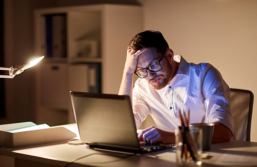 business, overwork, people, deadline and technology concept - stressed businessman in glasses with laptop computer thinking at night office