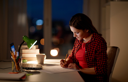 people, education, freelance and learning concept - woman or student girl with laptop computer writing to notebook at home at night