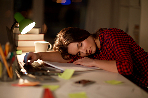 education, freelance, overwork and people concept - tired student woman sleeping on table at night home