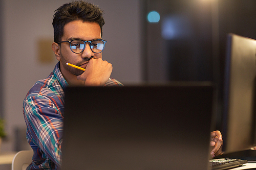 deadline, technology and people concept - close up of creative man in glasses working at night office and thinking