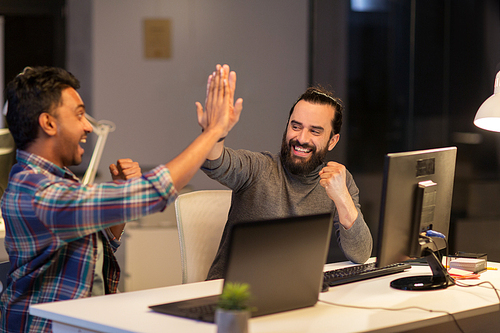 deadline, teamwork and success concept - creative team with computers making high five at night office