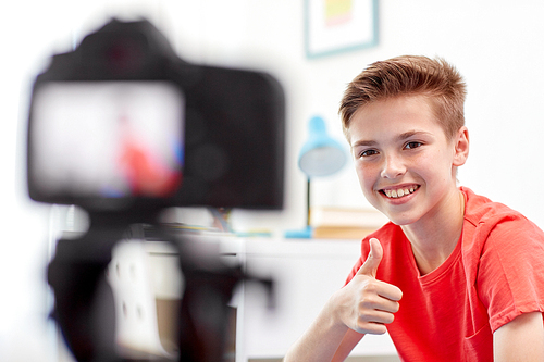 blogging, technology and people concept - happy smiling boy or . with camera recording video at home and showing thumbs up