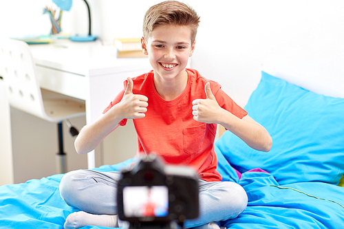 blogging, technology and people concept - happy smiling boy or . with camera recording video at home and showing thumbs up