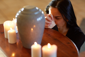 burial, people and mourning concept - sad woman with cinerary urn and candles praying at funeral in church