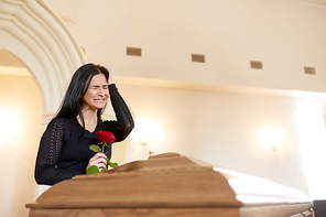 burial, people and mourning concept - crying unhappy woman with red rose and coffin at funeral in church