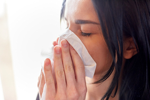 people, health and sadness concept - close up of unhappy woman with paper wipe blowing nose or crying
