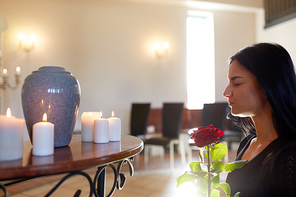 people and mourning concept - sad woman with red rose and cinerary urn at funeral in church