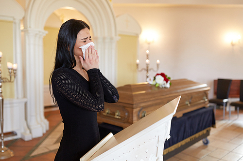 burial, people, grief and mourning concept - close up of sad woman with napkin crying near coffin at funeral in church