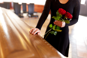 people and mourning concept - woman with red roses and coffin at funeral in church