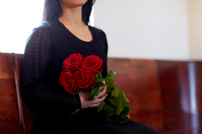 people, grief and mourning concept - close up of woman with red roses sitting on bench at funeral in church