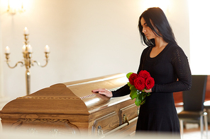 burial, people and mourning concept - unhappy woman with red rose and coffin at funeral in church