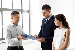 real estate business, sale and people concept - male realtor with clipboard and pen showing contract document to customers at new office room