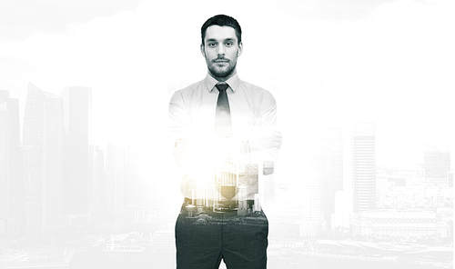 business and people concept - handsome businessman with crossed arms over city buildings and double exposure effect