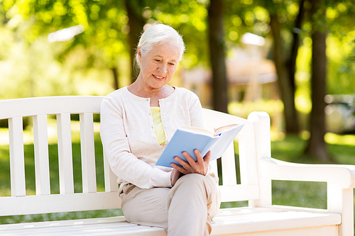 old age, retirement and people concept - happy senior woman reading book sitting on bench at summer park