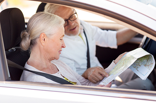 road trip, travel and old people concept - happy senior couple with map driving in car