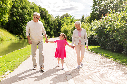 family, generation and people concept - happy smiling grandmother, grandfather and little granddaughter walking at park