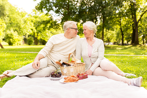 old age, holidays, leisure and people concept - happy senior couple with picnic basket sitting on blanket at summer park