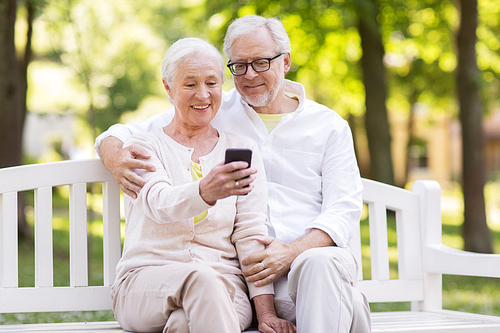 technology, relationship and old people concept - happy senior couple with smartphone taking selfie and hugging at park