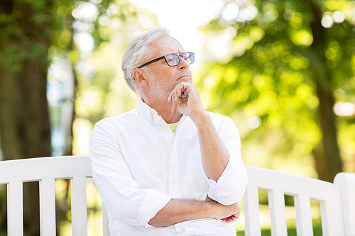 old age, retirement and people concept - thoughtful senior man in glasses sitting on bench at summer park