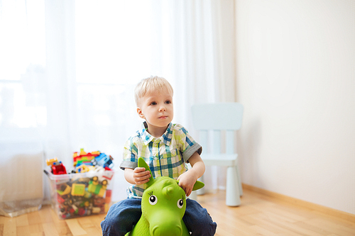 childhood, toys and people concept - happy little baby boy playing with ride-on toy horse at home