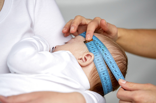 people, medical exam, healthcare and child care concept - close up of hands with tape measuring baby head