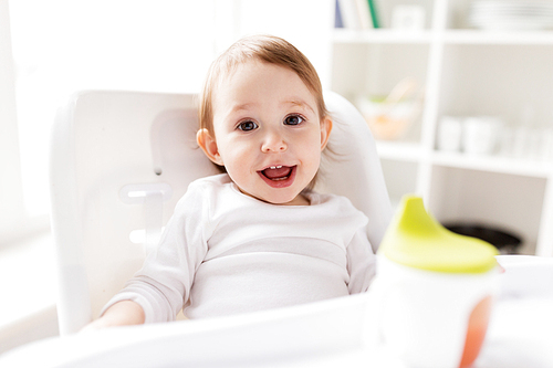 childhood and people concept - happy smiling little baby sitting in highchair at home