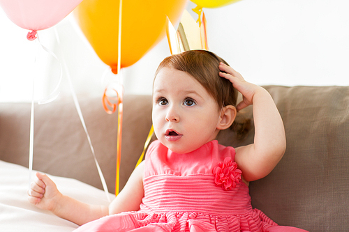 childhood, people and celebration concept - happy baby girl wearing crown on birthday party at home