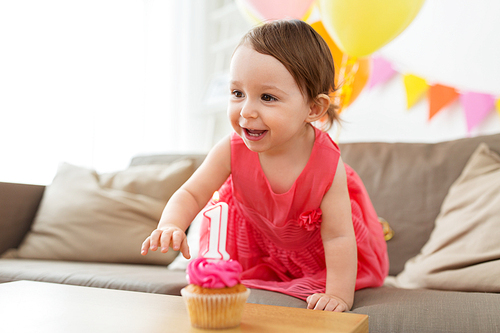childhood, people and celebration concept - happy baby girl with cupcake on birthday party at home