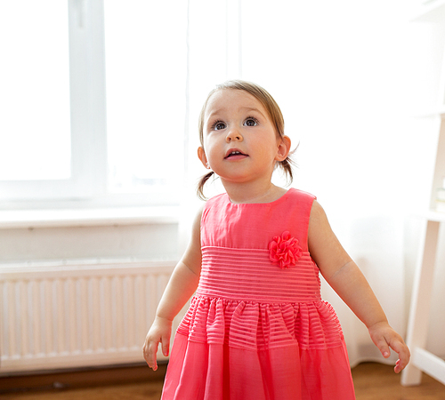 childhood and people concept - happy baby girl in pink dress at home