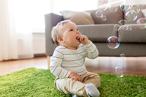 childhood, kids and people concept - lovely baby boy playing with soap bubbles at home