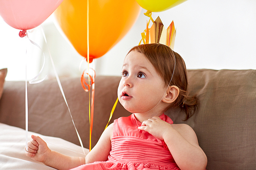 childhood, holidays and people concept - happy baby girl air balloons wearing princess crown on birthday party at home
