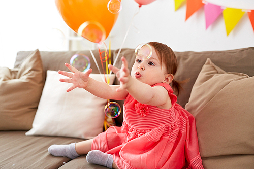 childhood, holidays and people concept - happy baby girl playing with soap bubbles on birthday party at home