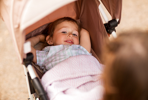 childhood, rest and people concept - happy little child or baby lying in stroller outdoors
