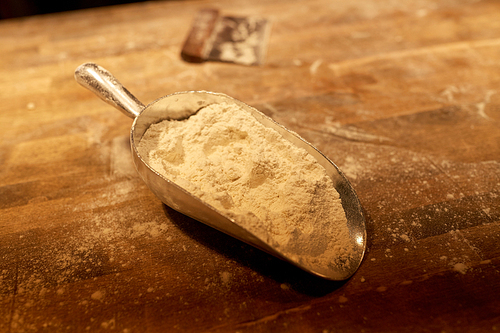 food, cooking and baking concept - flour in bakery scoop and dough cutter on wooden kitchen table