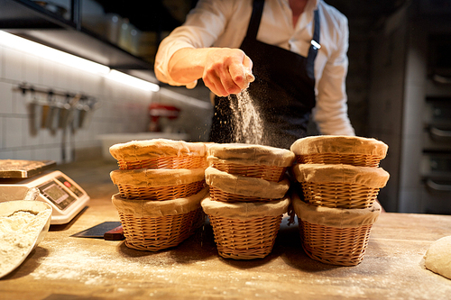 food cooking, baking and people concept - chef or baker preparing baskets while dough rising at bakery kitchen